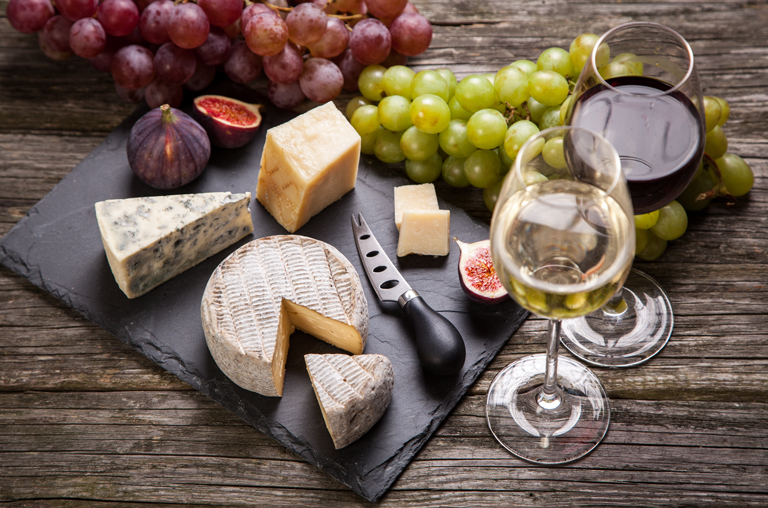 Gereifter Käse von Ziege und Schaf auf einer Schieferplatte, im Hintergrund ein Glas Rotwein und eine Karaffe